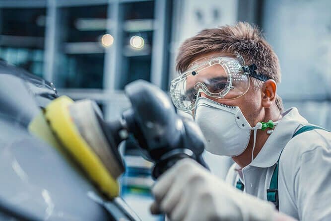 Tecnico con maschera e occhiali durante la lucidatura di una carrozzeria